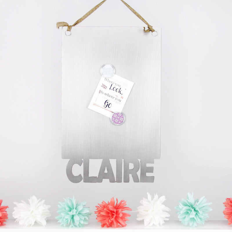 Rectangle magnetic board with name etched at the bottom, hanging on wall above pastel decorations.