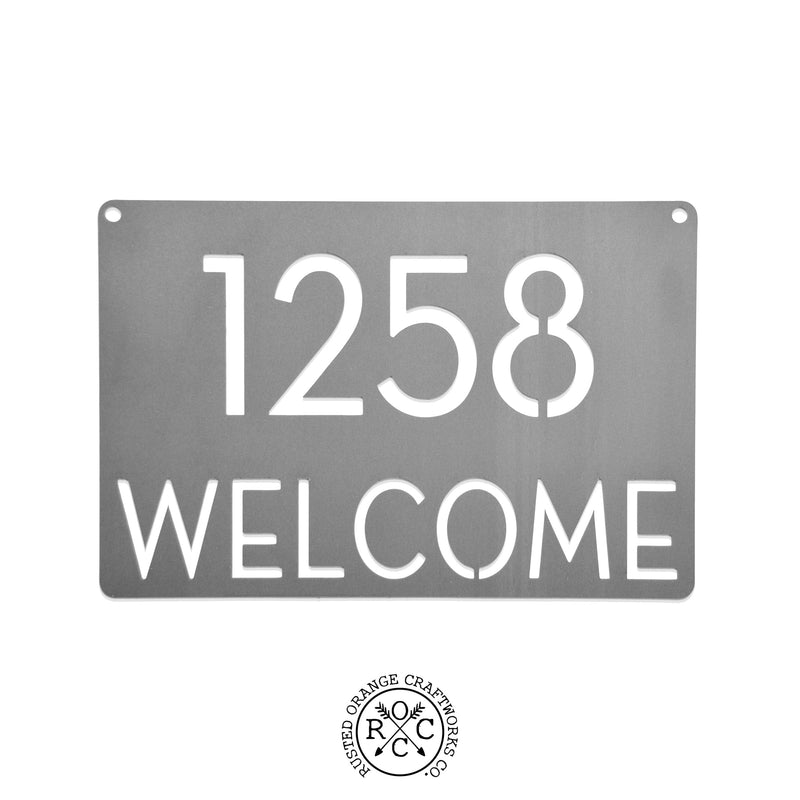 Metal rectangle welcome sign with house number, against white background.