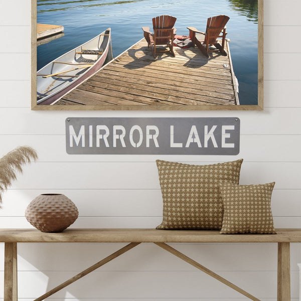 Rectangle metal sign with location name hanging on wall below photographs.