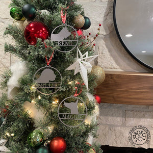 Round metal ornaments with personalized dog name and breed silhouette, hanging on Christmas tree.