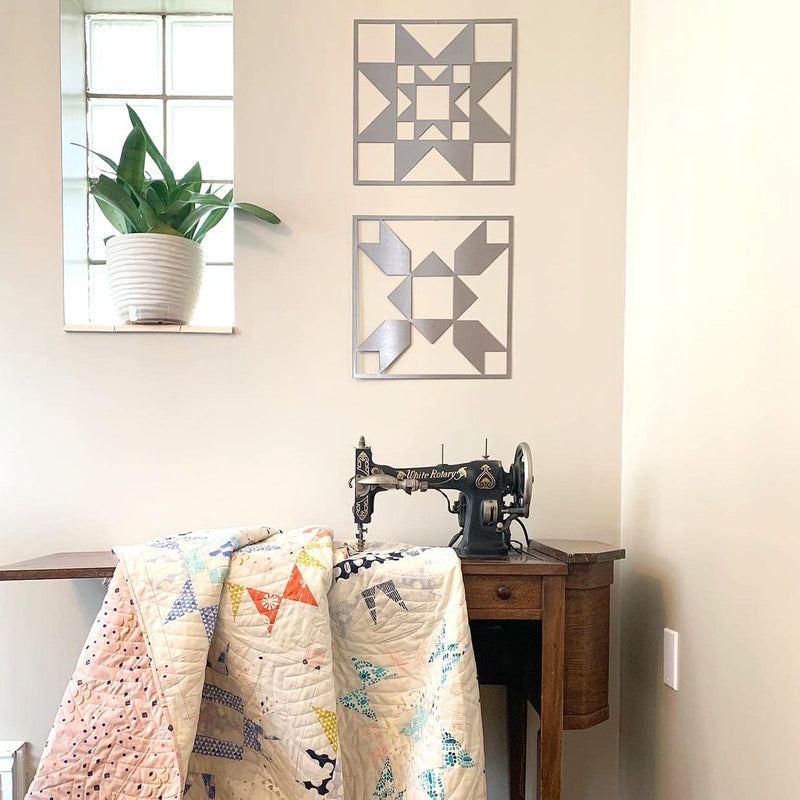 Two metal quilt block design squares hanging on wall above sewing machine table.
