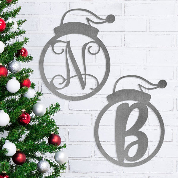 2 round metal decorations with monogram in center and santa hat on top hanging on wall next to Christmas tree.