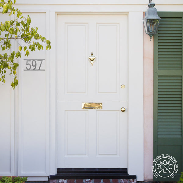 Home exterior with hanging custom metal address number next to front door.