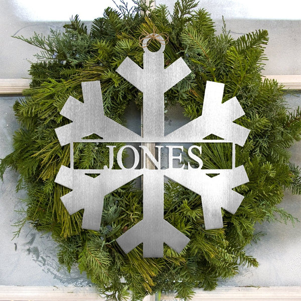 Metal snowflake with last name in center within pine wreath.
