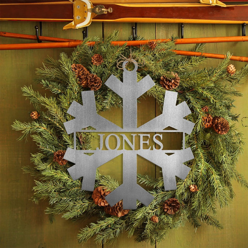 Metal snowflake with last name in center hanging with green wreath.