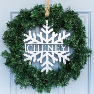 Metal snowflake with last name in center hanging with green wreath on front door.
