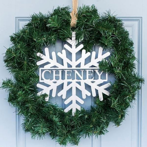 Metal snowflake with last name in center hanging with green wreath on front door.