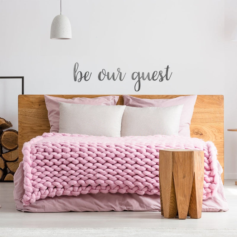 be our guest sign on wall above bed