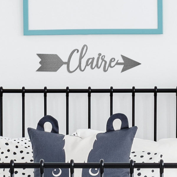 Metal arrow with name etched in center hanging on wall above baby crib.
