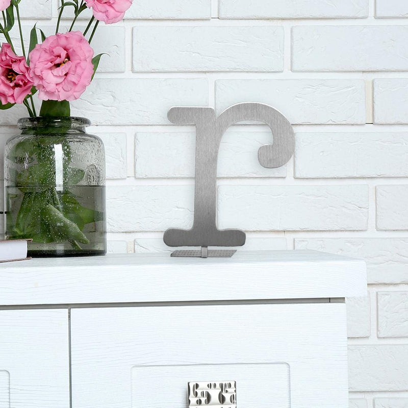 Letter R metal decoration standing on shelf next to pink flowers.