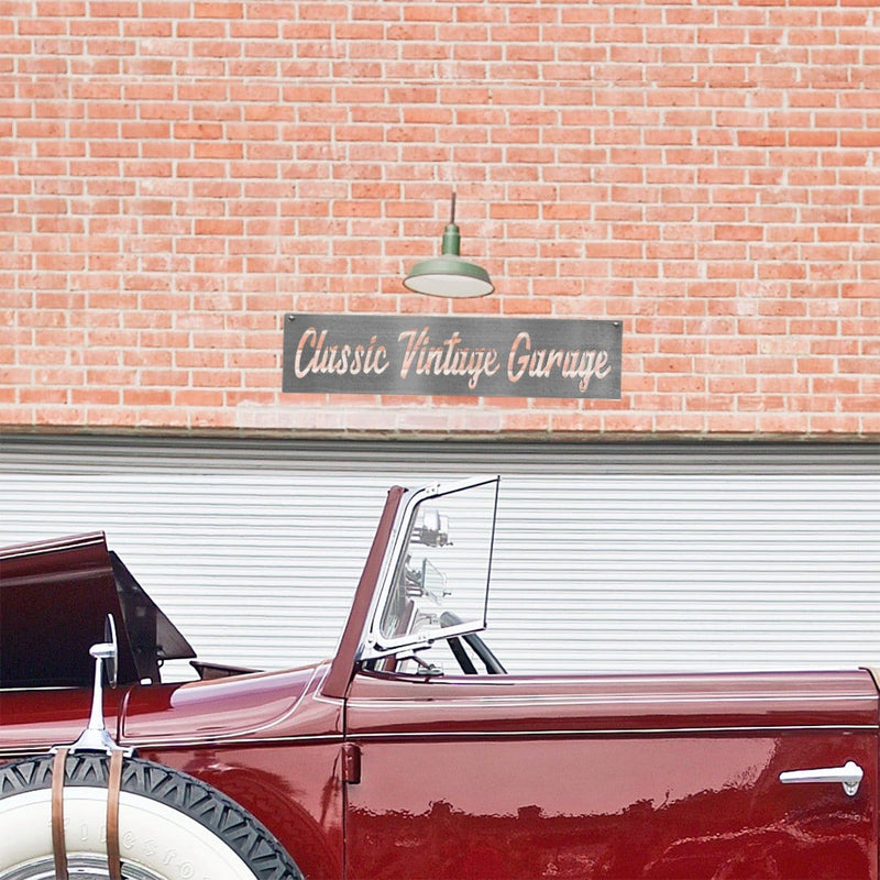 Rectangle metal sign saying Classic Vintage Garage hanging outside on brick wall above red convertible car.