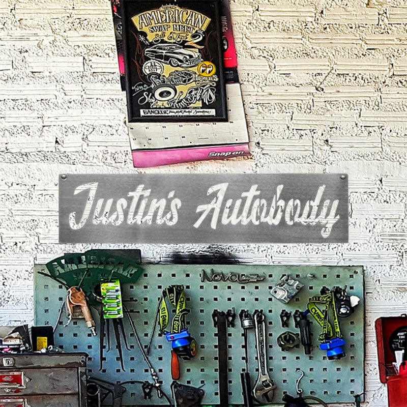 Rectangle metal sign saying Justin's Autobody hanging on wall above various tools.