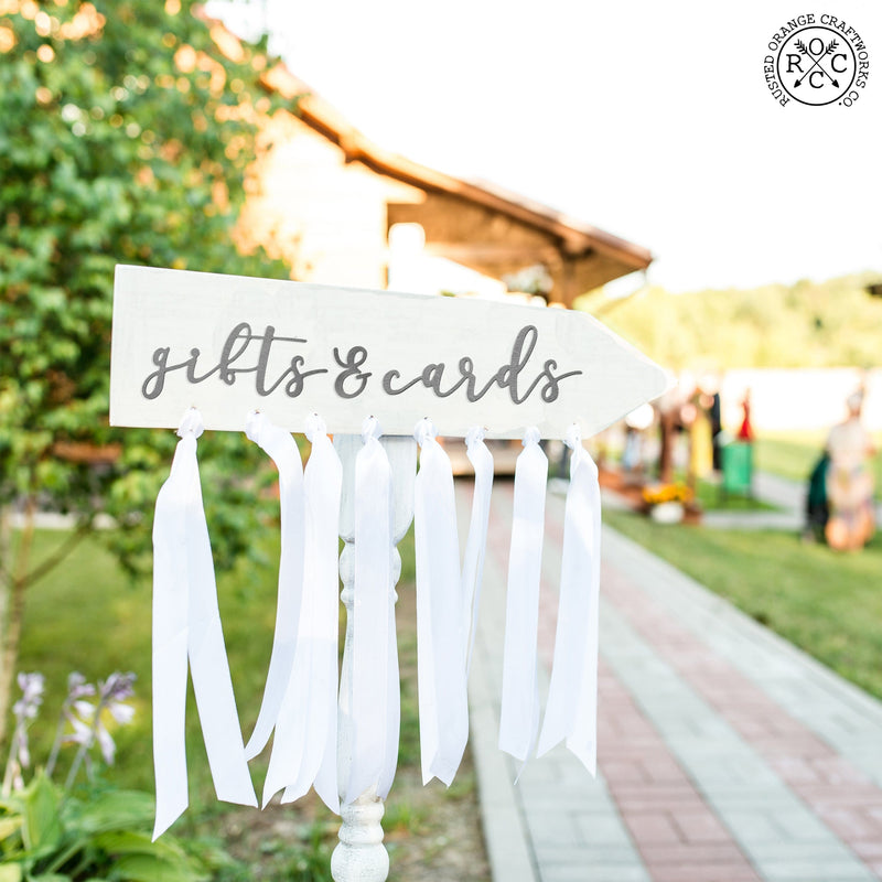 White arrow with metal words saying gifts & cards, white streamers hanging under arrow.