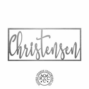 Metal cursive family name sign within rectangle against white background.