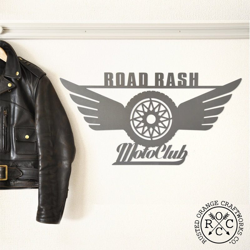 Leather jacket hanging next to hanging metal motorcycle sign which says Road Rash MotoClub