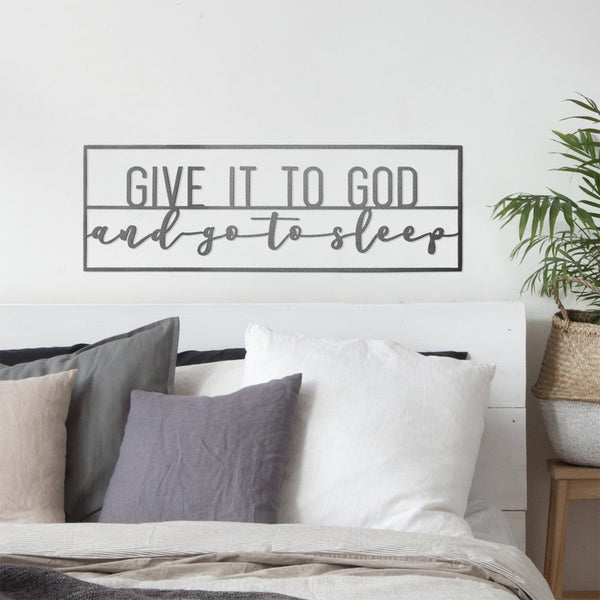Metal rectangle sign saying give it to god and go to sleep, hanging on wall above bed.